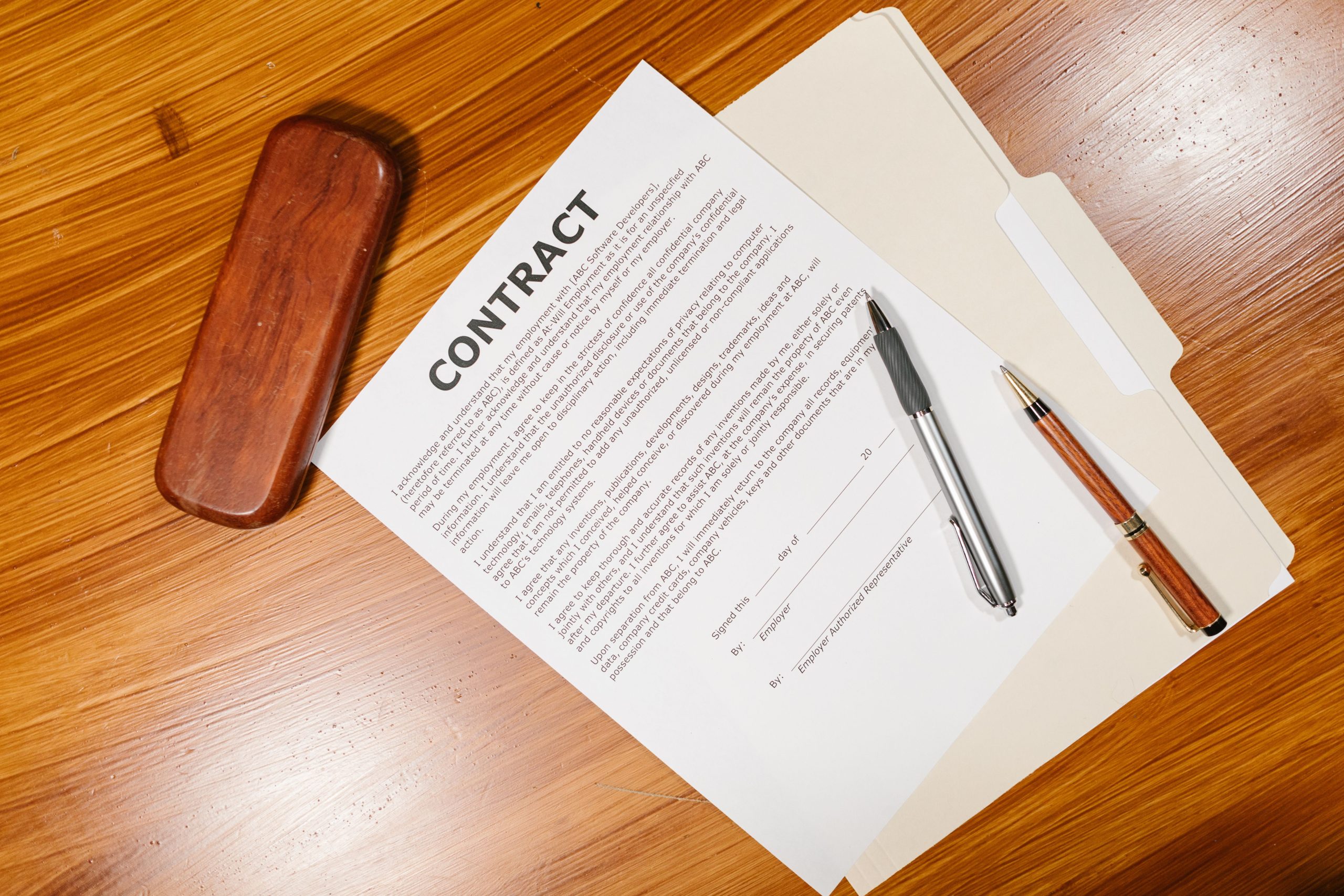 High-angle view of a contract document with pens and a case on a wooden table