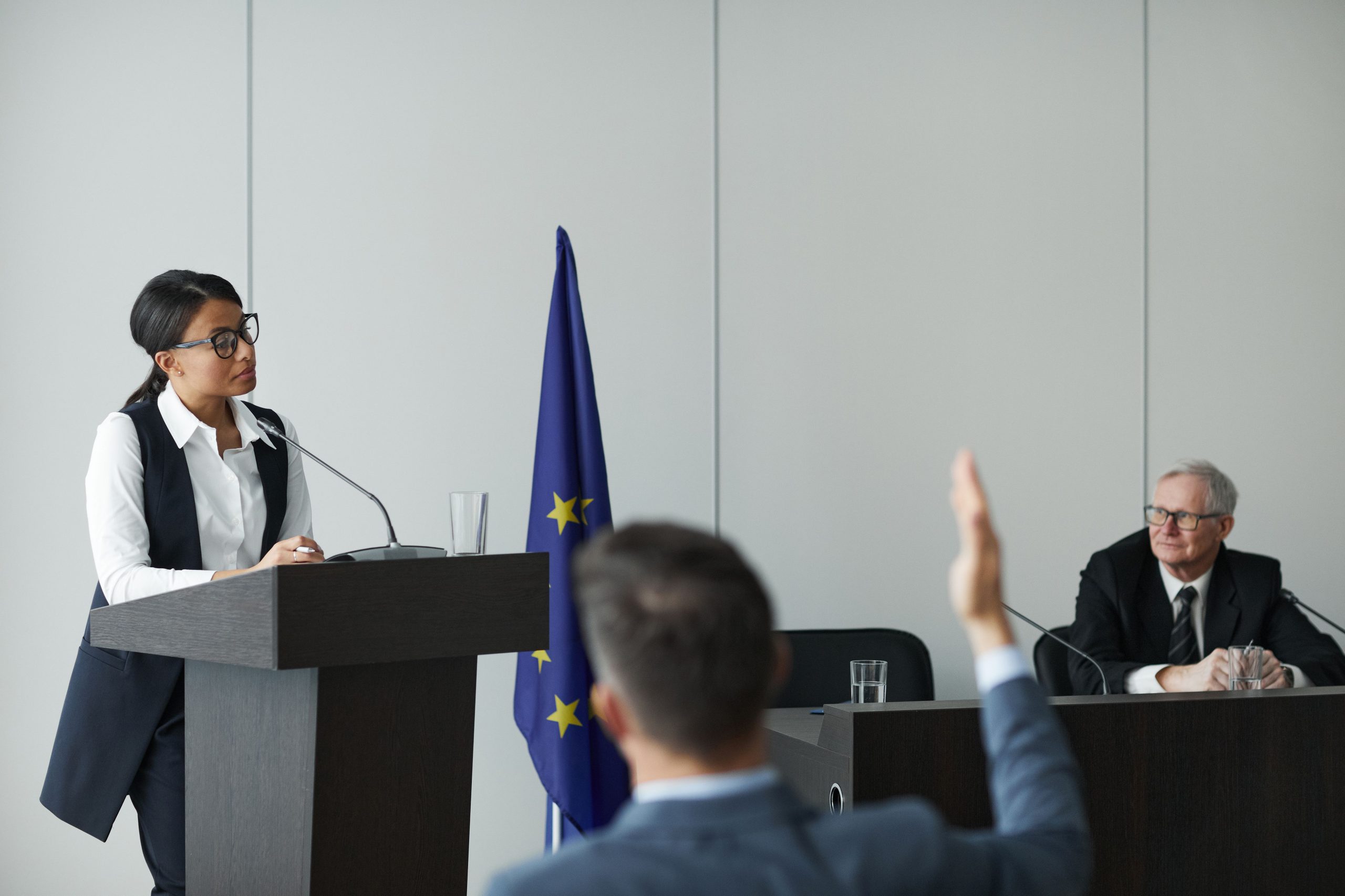 Woman speaking at a regional policy conference while delegates listen, illustrating leadership transition and public decision-making.
